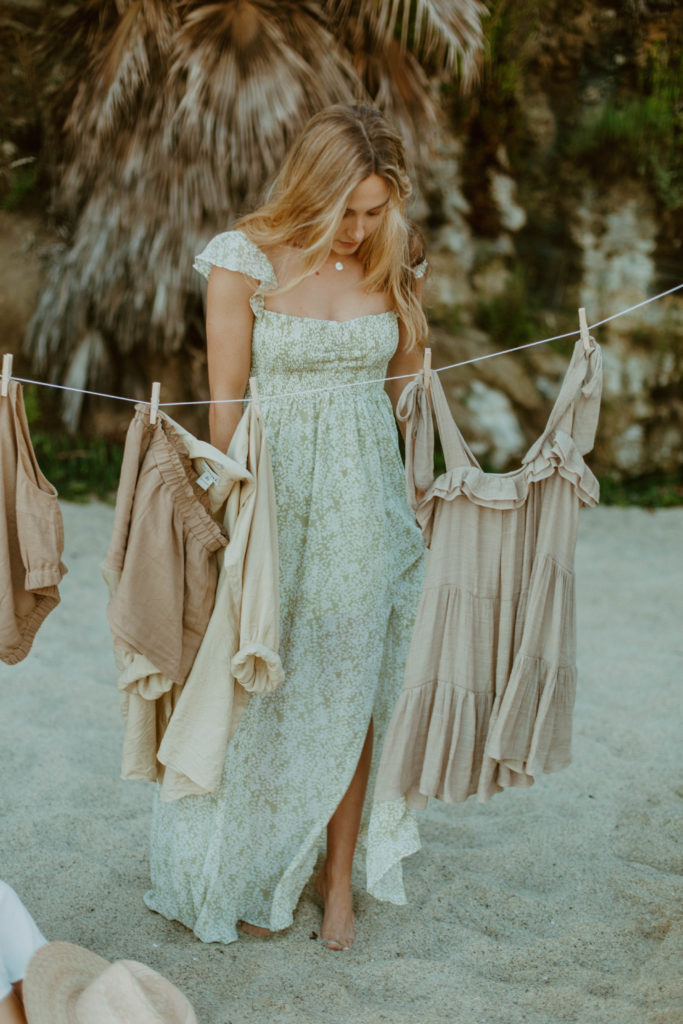 model is looking down at flowy, boho dress and other boho clothes hanging on clothes line