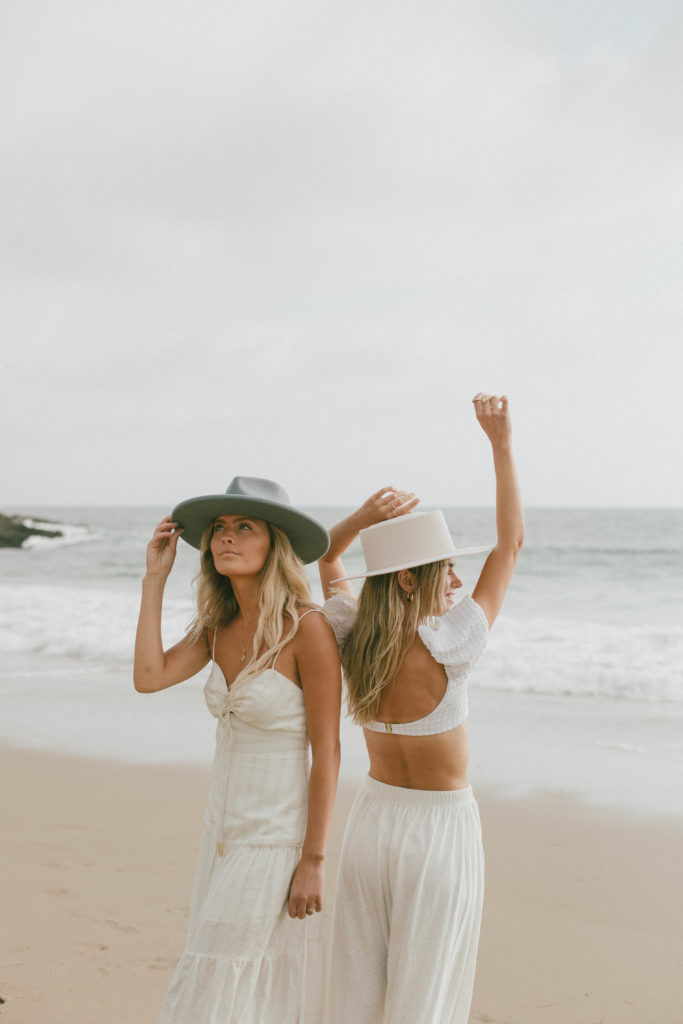 models are both posing on the beach with hats on