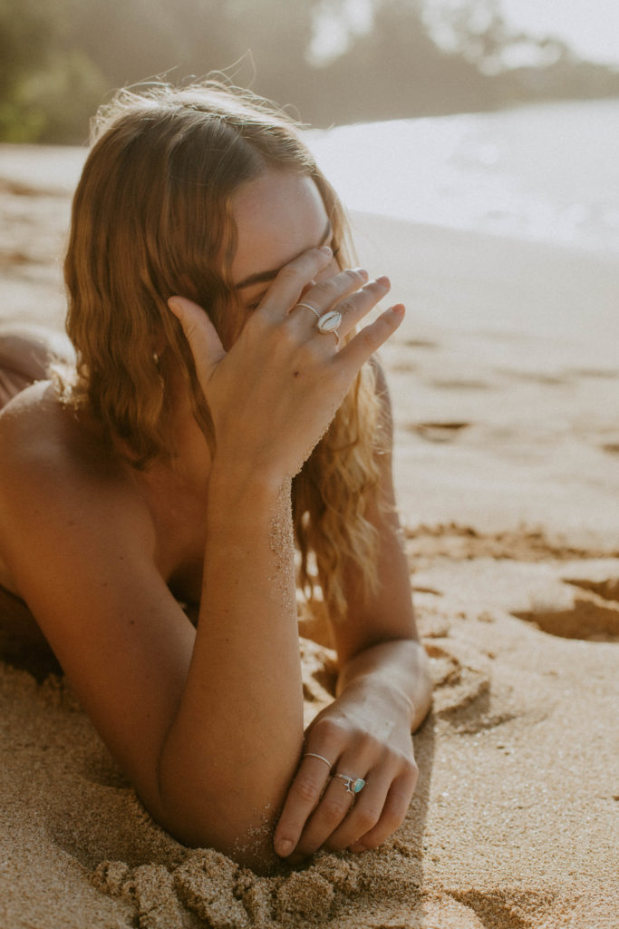 model is laying down in the sand, showcasing a sea shell ring