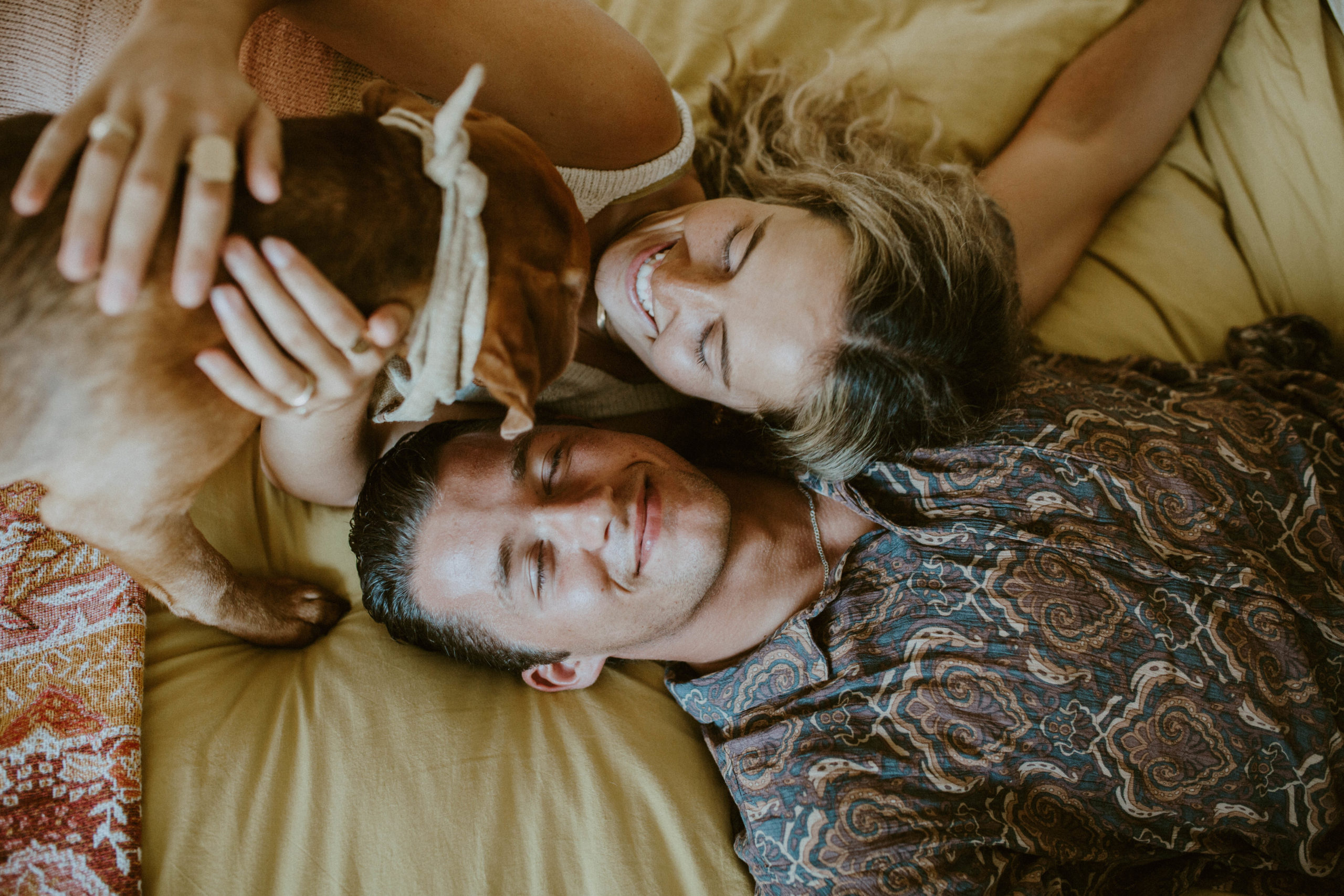 couple is laying down on bed with their dog