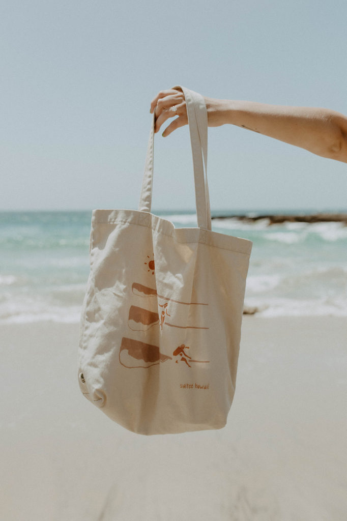 portrait of models hand holding a saltee hawaii graphic tote bag in hand 