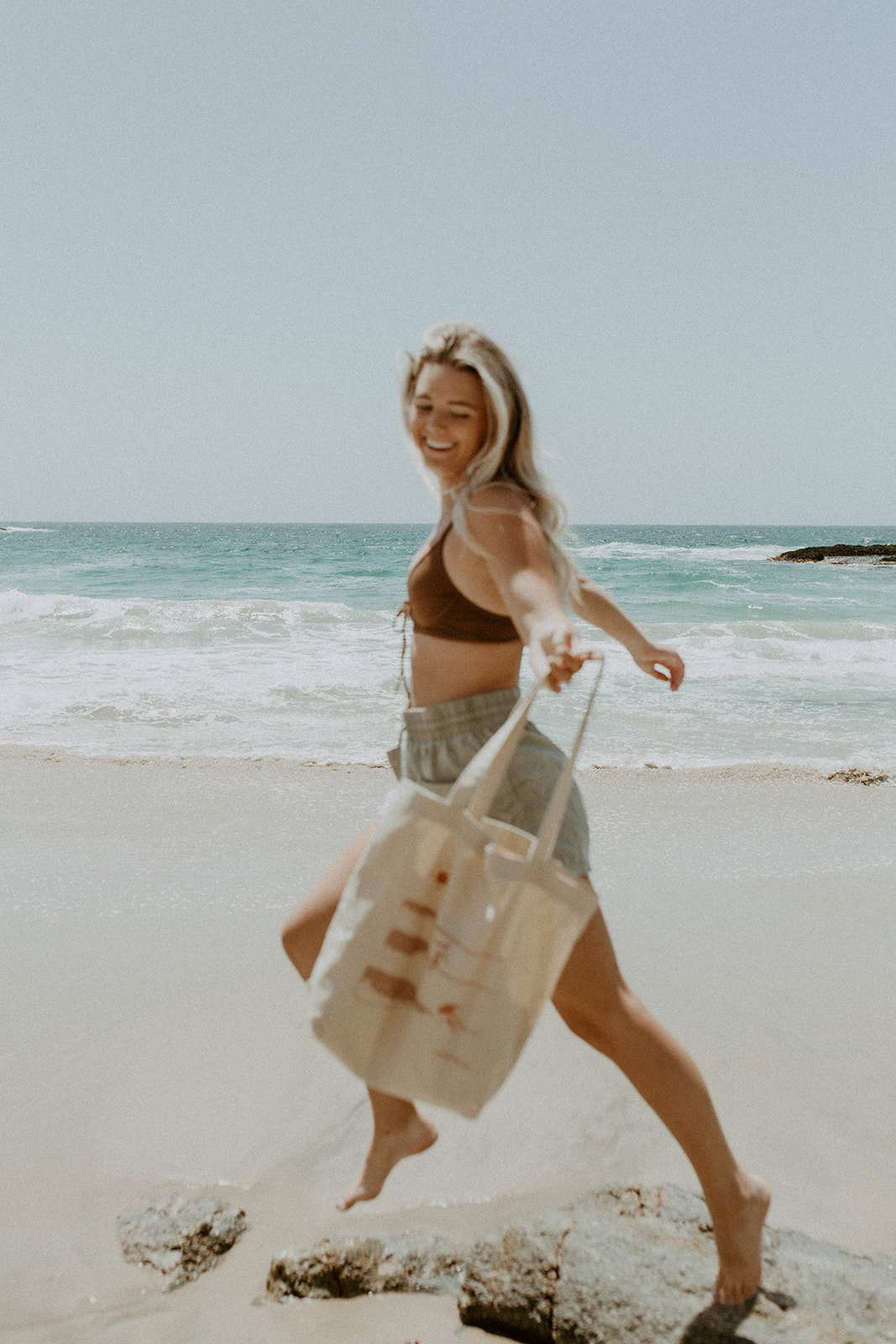model is running across beach with saltee hawaii graphic tote bag in hand