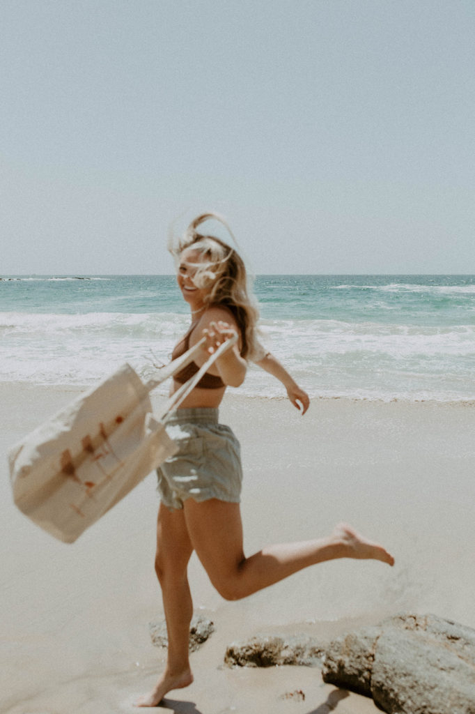 blurry candid of model running across the beach with saltee hawaii's graphic tote in hand