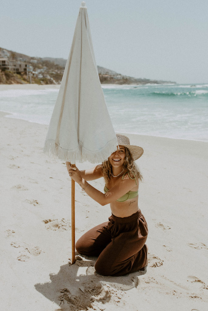 model is setting up a boho umbrella at the beach