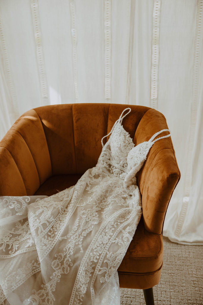 picture of the brides dress laying on a rust colored velvet chair