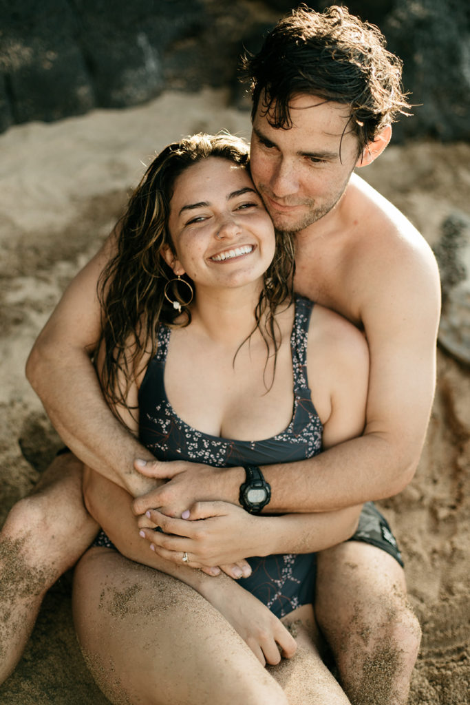 dani and her husband sitting in the sand and hugging each other