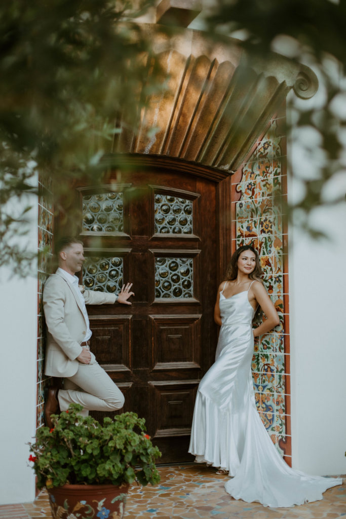 bride and groom are both leaning against a doorway of the adamson house and facing each other