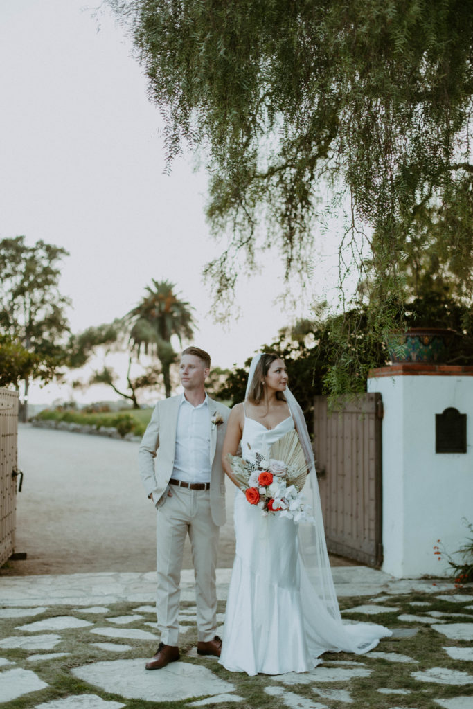bride and groom are standing on a cobblestone path and looking opposite ways at each other