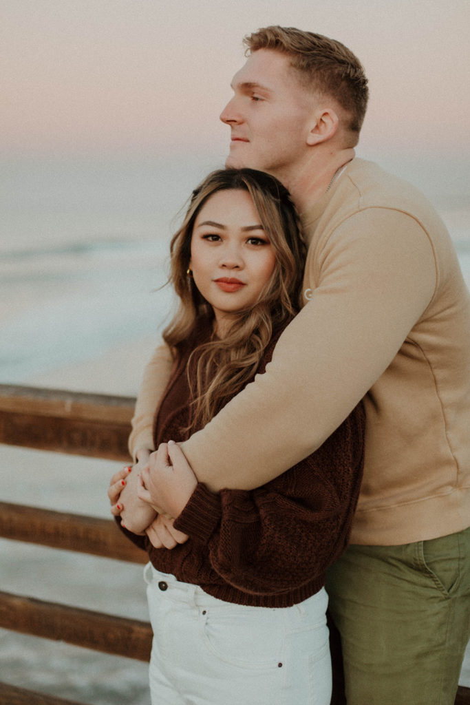 couple is standing on the pier and daniel has his arms wrapped around julianna