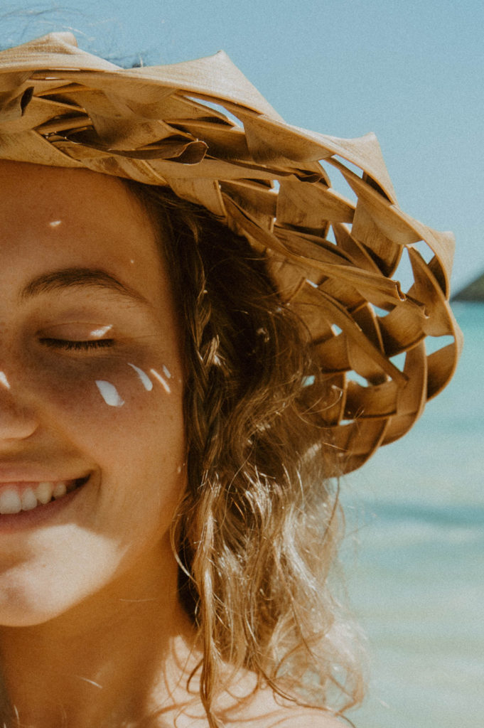 close up shot of models face as she is smiling and wearing a straw hat